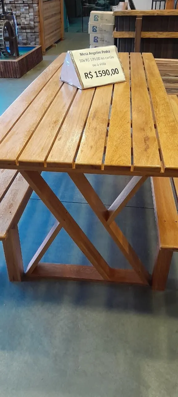 Detalhe da estrutura em X da mesa de madeira maciça, mostrando o acabamento artesanal